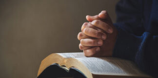Perseverança e fé em Deus foto de uma pessoa com a bíblia no colo e com as maos em cima e os dedos cruzados
