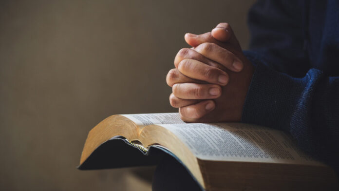 foto de uma pessoa com a bíblia no colo e com as maos em cima e os dedos cruzados